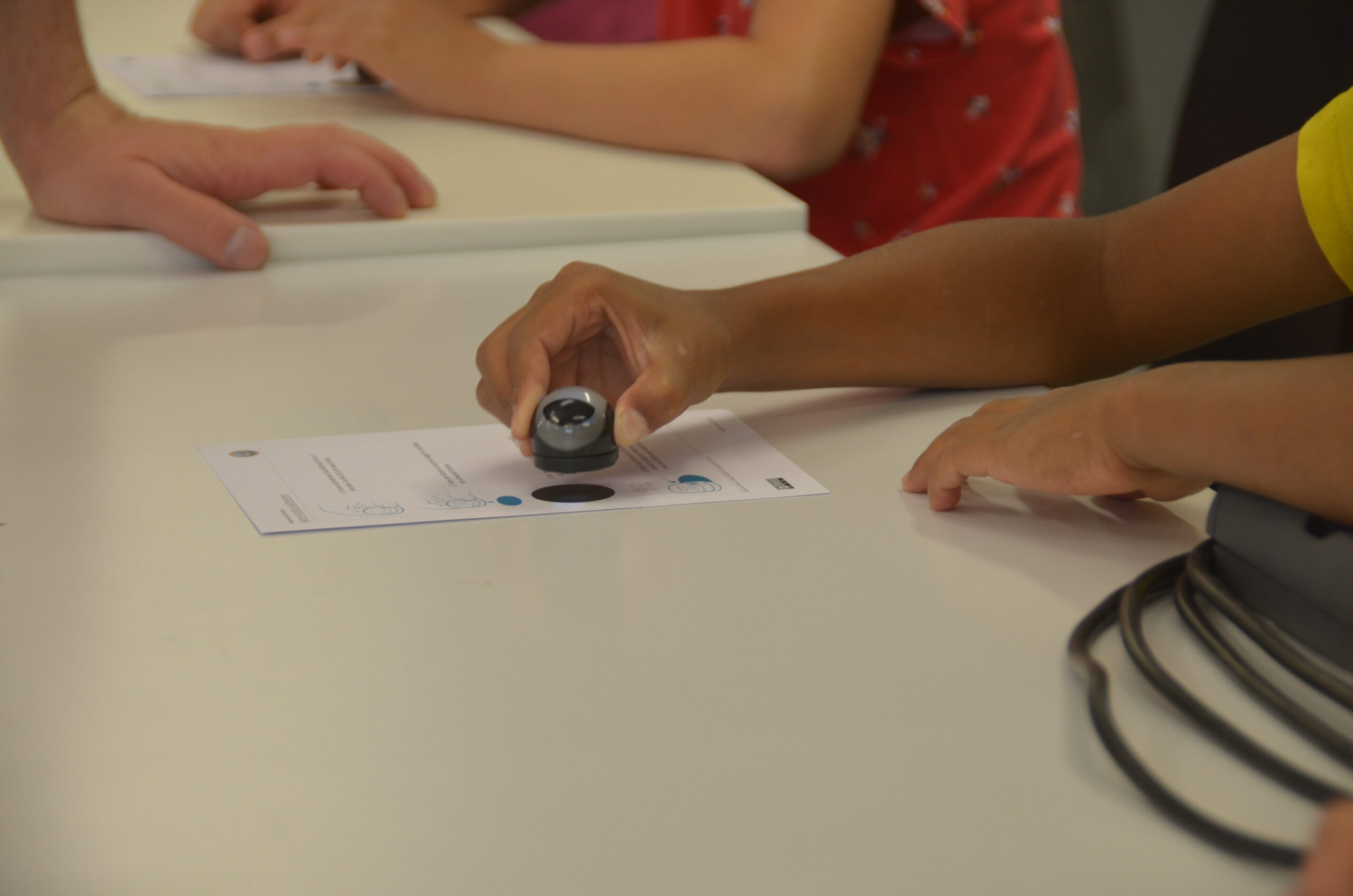 Hände platzieren einen kleinen Mini-Roboter auf einer Papier-Übungskarte.